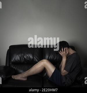 Dark filtered on stressful man sitting on sofa Stock Photo
