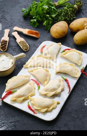 Frozen potato vareniki on marble serving board with ingredients Stock Photo