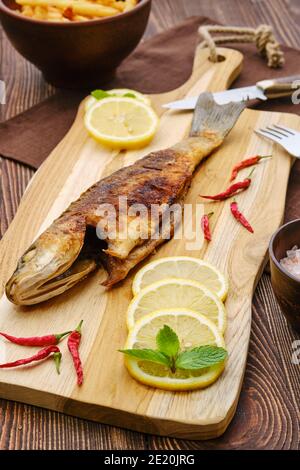 Fried sea bass with fried potato on wooden cutting board. Stock Photo