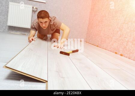 Young male repairman is laying panel of laminate floor indoors. Stock Photo