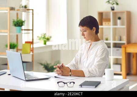 Young woman watching educational video or attending webinar using laptop computer Stock Photo