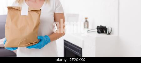 Young woman wearing medical mask receiving parcel from delivery indoors. Prevention of virus spread Stock Photo