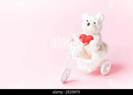 White bear on a bicycle holding a heart on a pink background with copy space Stock Photo