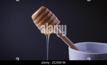 Honey wood dipper is pouring  honey. Honey dripping on white marble top. Healthy sweet ingredient for breakfast and pastry. Golden, yellow, raw honey. Stock Photo