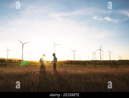 Investors and technician who are out of focus in the foreground are standing in talks about wind turbine power generation, Wind turbine farm is an alt Stock Photo