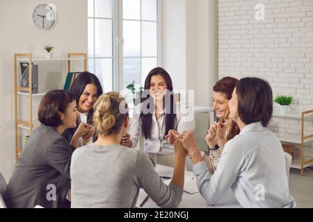 Team of happy young business women sitting around office table and holding hands Stock Photo