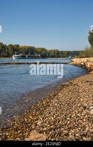 Ship sailing down the Rhine river next to a rocky shore on a summer day in Germany. Stock Photo