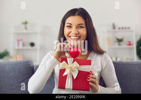 Happy young woman showing red heart and Valentine gift, smiling and saying thank you for present Stock Photo