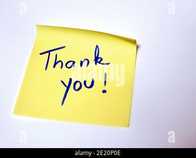 The sentence Thank you written by hand on a yellow post it and put on the white table Stock Photo