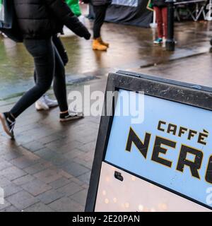 London UK, Anonymous People Or Shoppers Walking Past A Sign Board For Cafe Nero Coffee Shop On A Wet Winter Afternoon Stock Photo