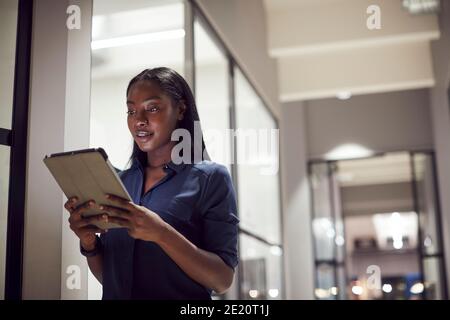 Evening Shot Of Businesswoman Standing In Corridor Of Modern Office Using Digital Tablet Stock Photo
