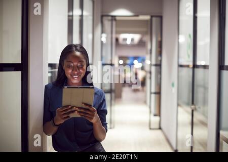 Evening Shot Of Businesswoman Standing In Corridor Of Modern Office Using Digital Tablet Stock Photo