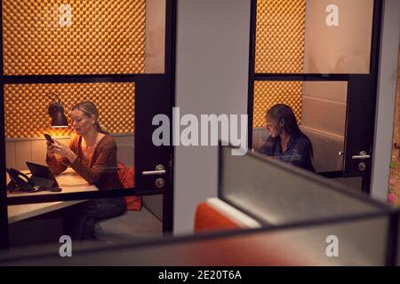 Businesswomen Working Late In Individual Office Cubicles Using Laptop And Digital Tablet Stock Photo
