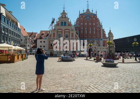 Riga, Latvia - 06.04.2018: Tourists in Town Hall Square, iconic meeting place in Riga. House of the Blackheads and sculpture of Saint Roland. Stock Photo