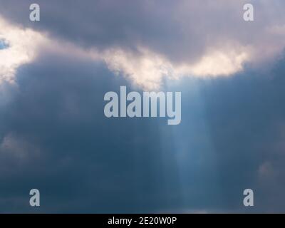 The sun's rays create a cone of light emanating from dense dark clouds Stock Photo