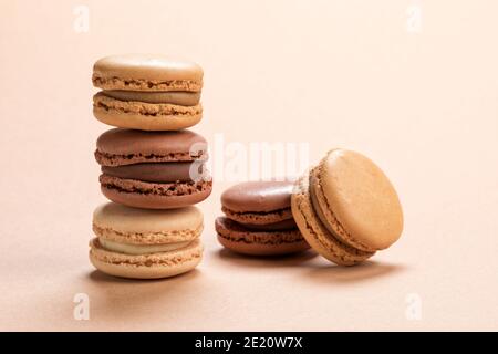 Stacked french macarons of coffee, vanilla and chocolate flavors on light brown background. Gourmet pastry closeup- Stock Photo