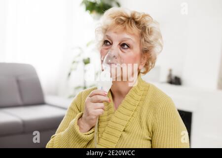 Elderly woman using asthma machine on light background Stock Photo
