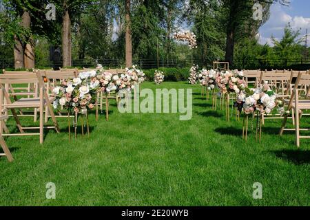 White wooden empty chairs in a row and flowers bouquets on a green grass. Wedding ceremony decorations. Stock Photo