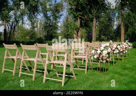 White wooden empty chairs in a row and flowers bouquets on a green grass. Wedding ceremony decorations. Stock Photo