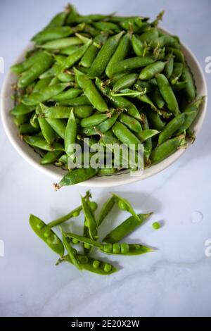 Peas. Green pea pods in a plate on a white table. Harvest. Healthy food close-up. Copy space Stock Photo