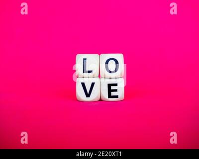 Love word written on wood block on pink red background, minimal style. Love, text is written in black letters on wooden cubes. Stock Photo