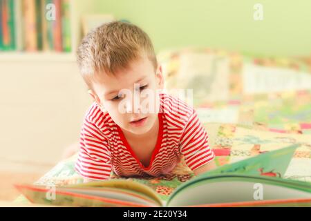 Cute little boy reading alphabet book while laying on bed. Child looks at open book. Homeschool lesson Stock Photo