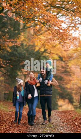 Family Walking Along Autumn Woodland Path With Father Carrying Son On Shoulders Stock Photo
