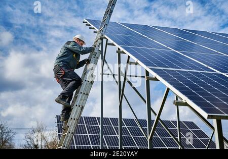 Technician getting down the ladder after installing photovoltaic solar panels on a sunny day. Renewable energy resource. Concept of alternative energy and power sustainable resources. Stock Photo