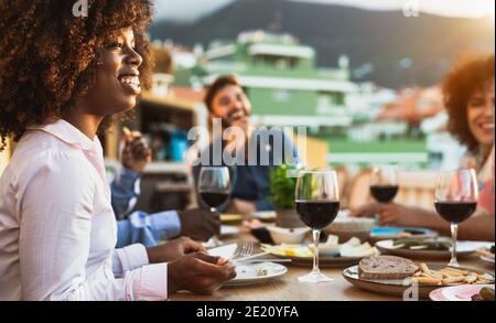 Young multiracial friends doing appetizer and drinking red wine on house patio during sunset time Stock Photo