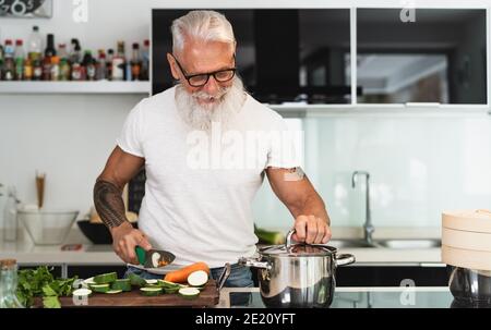 Happy senior man having fun cooking at home - Elderly person preparing health lunch in modern kitchen Stock Photo