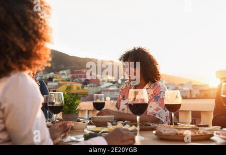 Young multiracial friends doing appetizer and drinking red wine on house patio during sunset time Stock Photo
