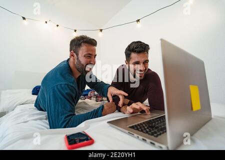 Happy gay men couple using laptop in bed - Homosexual love and gender equality in relationship concept Stock Photo