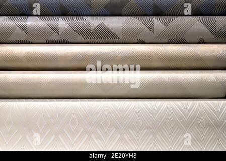 Rolled up rolls of vinyl wallpaper. Different textures and colors, as background. Beige, gray wallpapers with abstract patterns for the wall Stock Photo