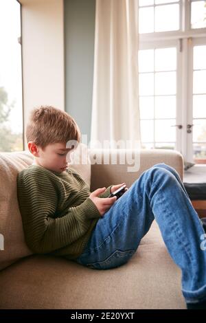 Young Boy On Sofa At Home Having Fun Playing Game On Mobile Phone Stock Photo