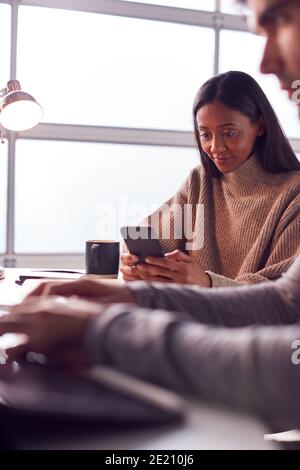 Businessman Working On Laptop At Desk Collaborating With Female Colleague Using Mobile Phone Stock Photo