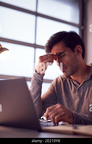 Tired Businessman Working Late Using Laptop At Desk In Office Rubbing Eyes Stock Photo