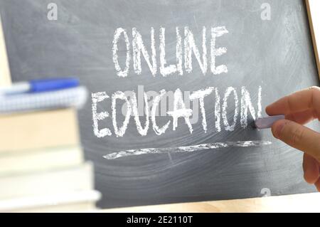 Teacher writing on a blackboard the word 'Online Education' in a online class. Some books and school materials. Stock Photo