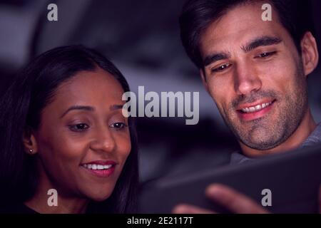 Businessman And Businesswoman Working Late Using Digital Tablet With Faces Illuminated Stock Photo