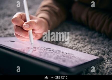 Close Up Of Woman Drawing On Digital Tablet Using Stylus Pen Lying On Carpet At Home Stock Photo
