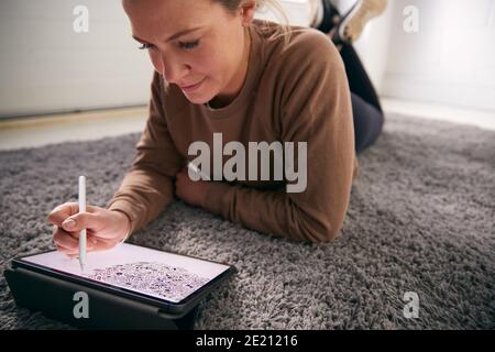 Woman Drawing On Digital Tablet Using Stylus Pen Lying On Carpet At Home Stock Photo