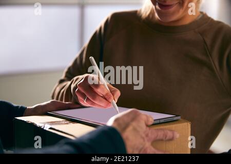 Woman Signing For Courier Delivery To Office Using Digital Tablet Stock Photo