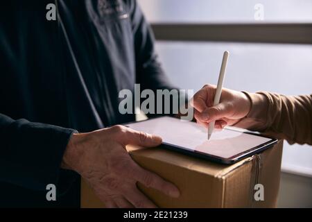 Woman Signing For Courier Delivery To Office Using Digital Tablet Stock Photo