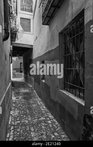 Vertical grayscale shot of narrow pathway between stone wall building ...