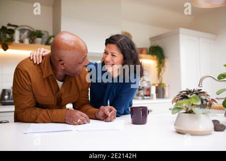 Mature Couple Reviewing And Signing Domestic Finances And Investment Paperwork In Kitchen At Home Stock Photo