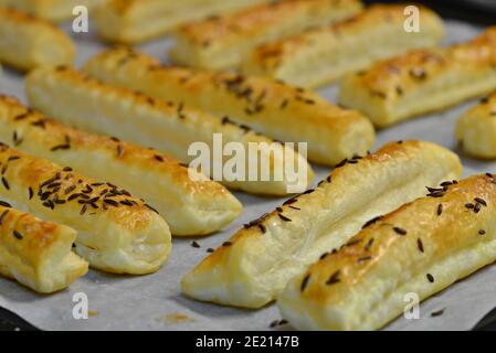 Baked salty sticks with salt and cumin. Golden baked savory pastry. Home baking appetizers. Crispy savory pastry on a baking sheet. Stock Photo
