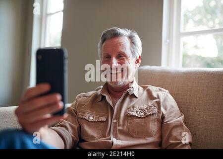 Mature Man At Home Self Isolating During Lockdown Making Video Call On Mobile Phone Stock Photo