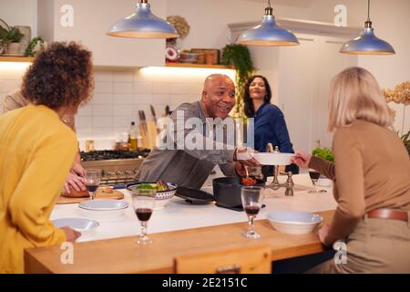 Group Of Mature Friends Meeting At Home Serving Food At Dinner Party And Drinking Wine Together Stock Photo