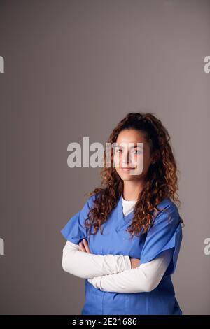 Studio Portrait Of Young Female Nurse Wearing Scrubs Standing Against Grey Background Stock Photo