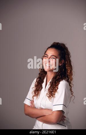 Studio Portrait Of Young Female Nurse Wearing Uniform Standing Against Grey Background Stock Photo