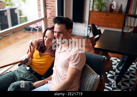 Loving Couple Sitting On Sofa At Home Watching TV And Relaxing Together Stock Photo
